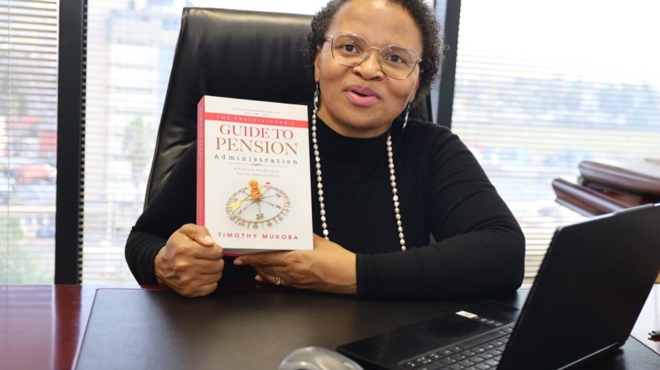 A woman at her desk holding a copy of The Practitioner's Guide to Pension Administration.