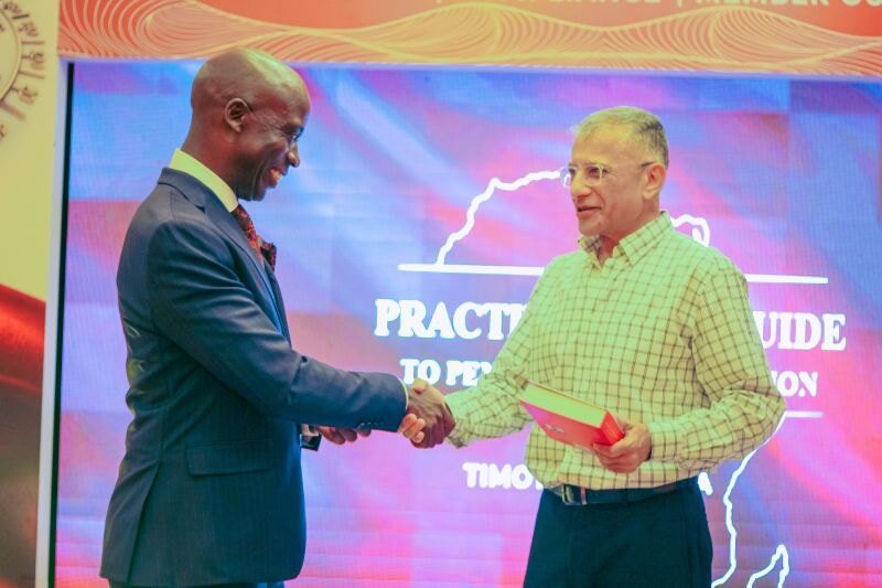 A handshake on stage at the launch, in front of the book’s backdrop.