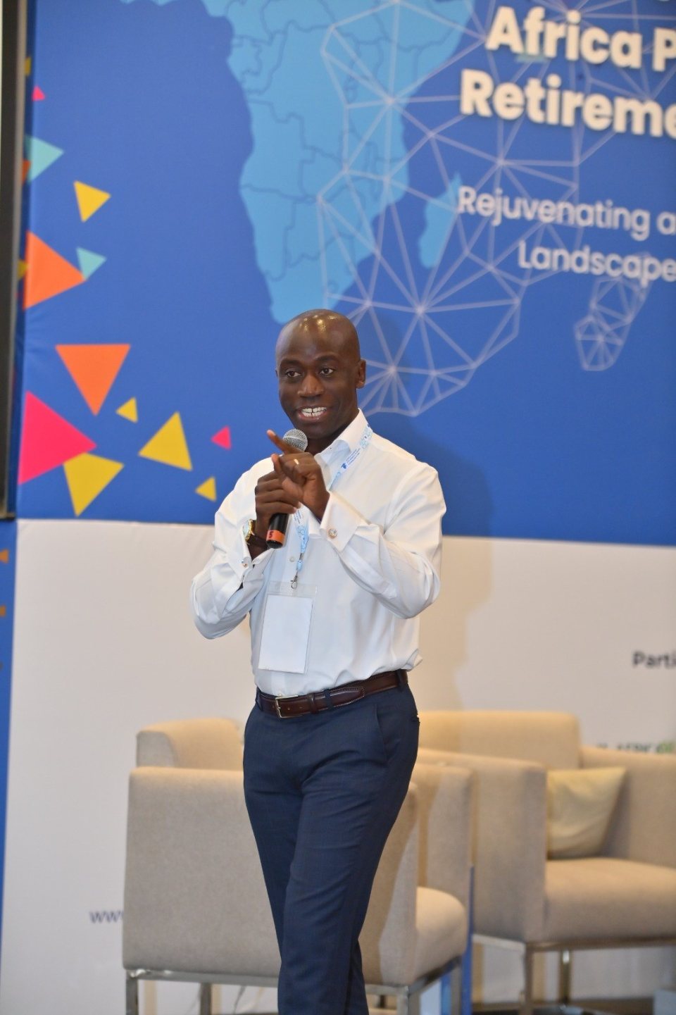 Timothy Mukoba speaking into a microphone on stage at the Africa Pension Funds & Retirement Summit, in front of the summit banner.